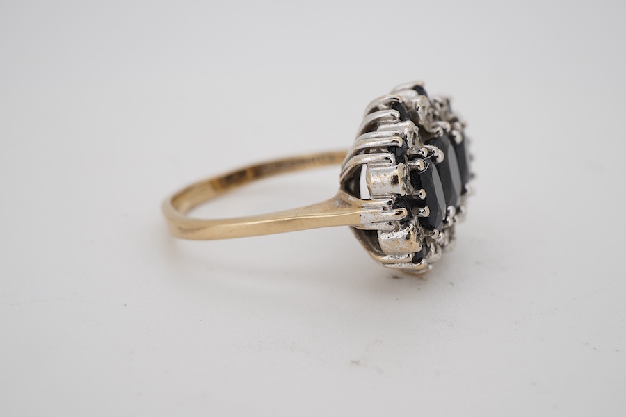 A modern 9ct gold and three stone sapphire set dress ring, with sapphire and diamond chip set border, size Q.